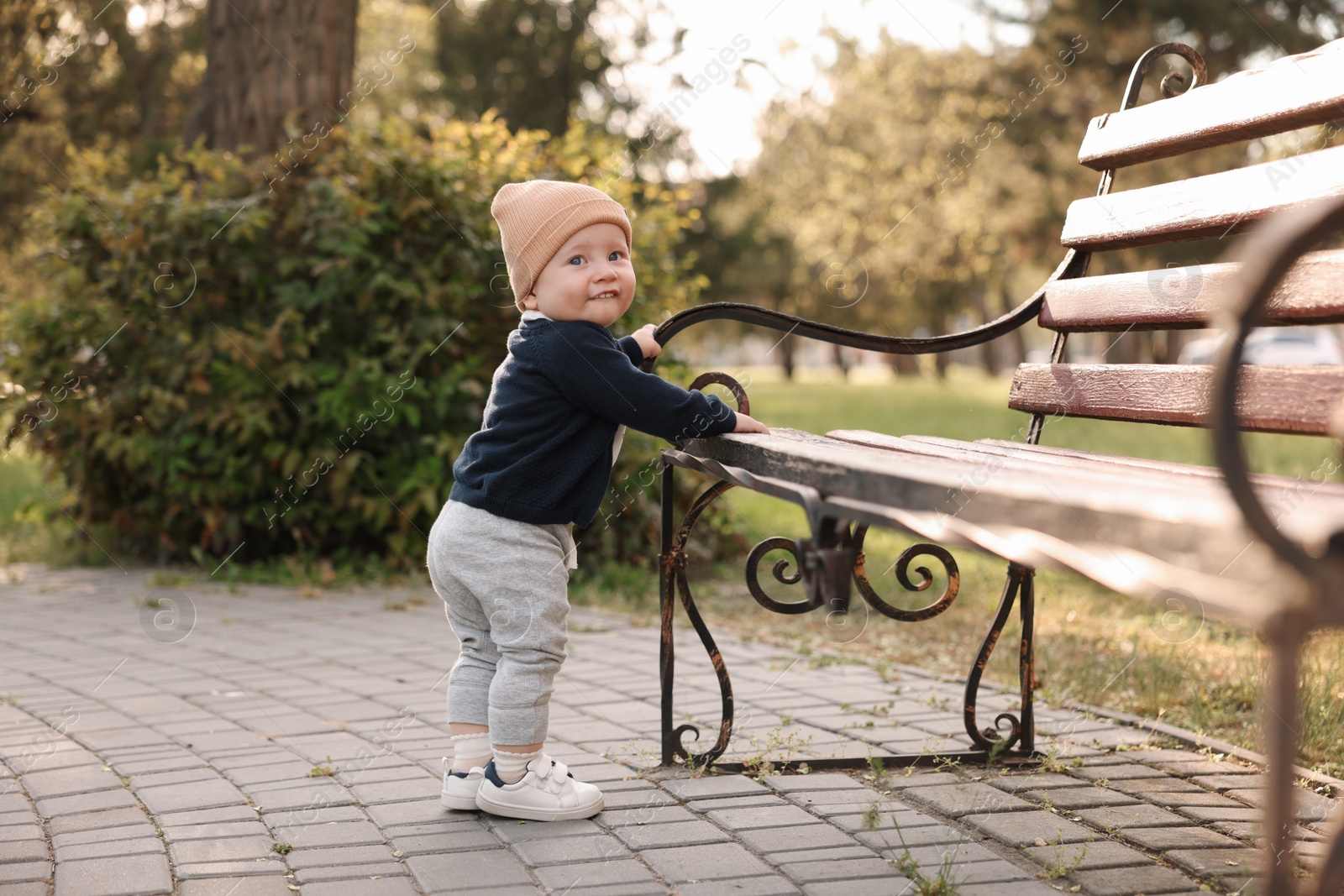 Photo of Little baby learning to walk near bench in park