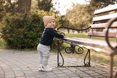 Little baby learning to walk near bench in park