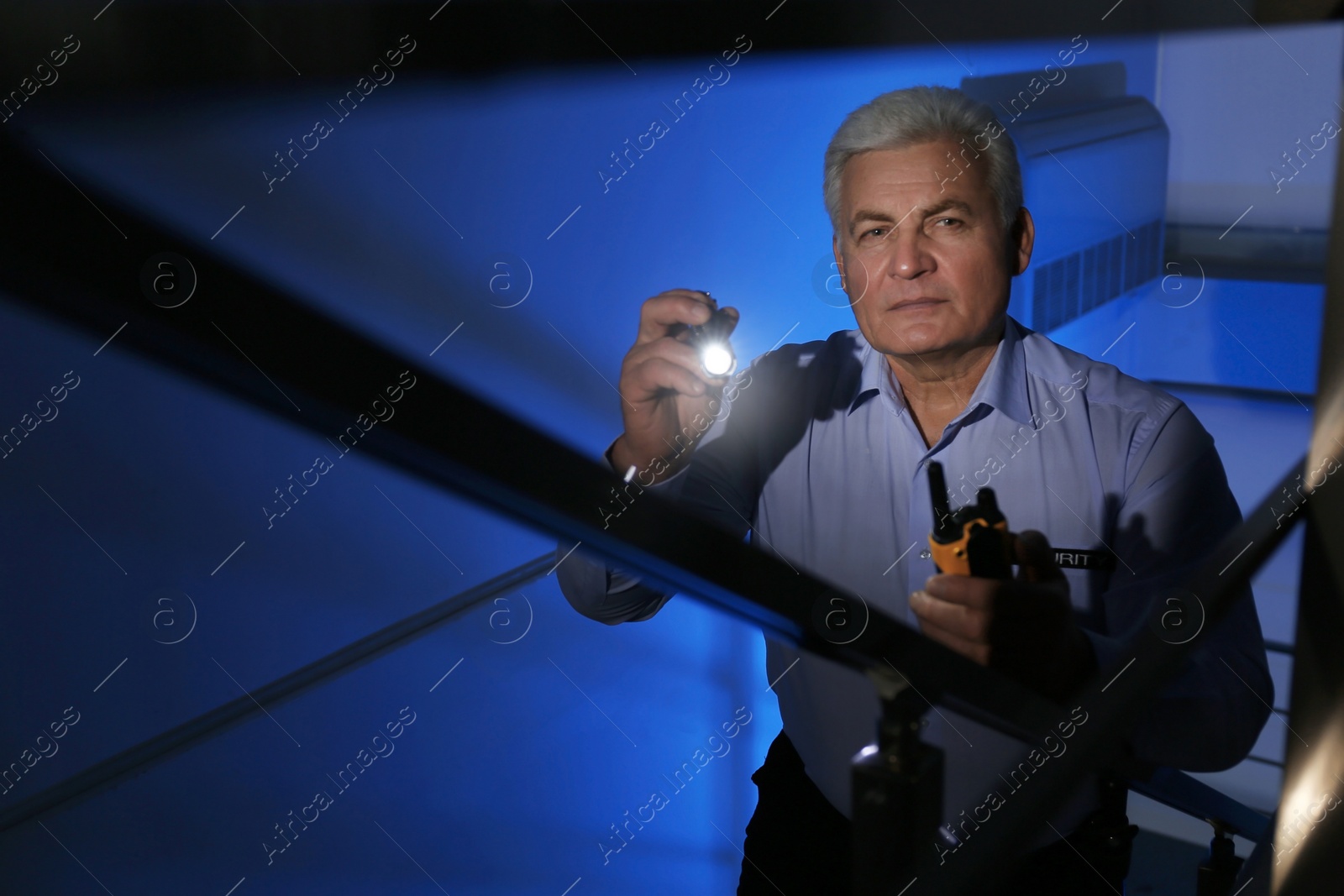 Photo of Professional security guard with flashlight on stairs in dark room
