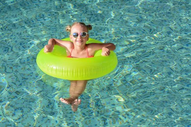 Photo of Happy little girl with inflatable ring in outdoor swimming pool on sunny day, space for text
