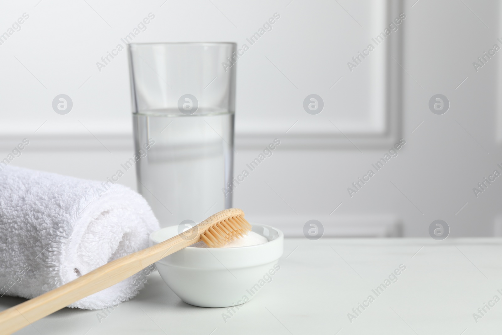 Photo of Bamboo toothbrush, bowl of baking soda, towel and glass of water on white table. Space for text