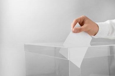 Photo of Man putting his vote into ballot box on light background, closeup