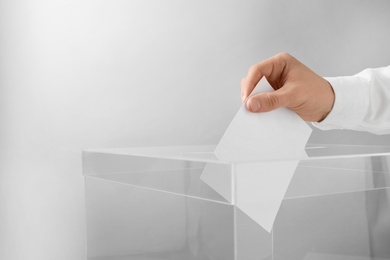 Man putting his vote into ballot box on light background, closeup