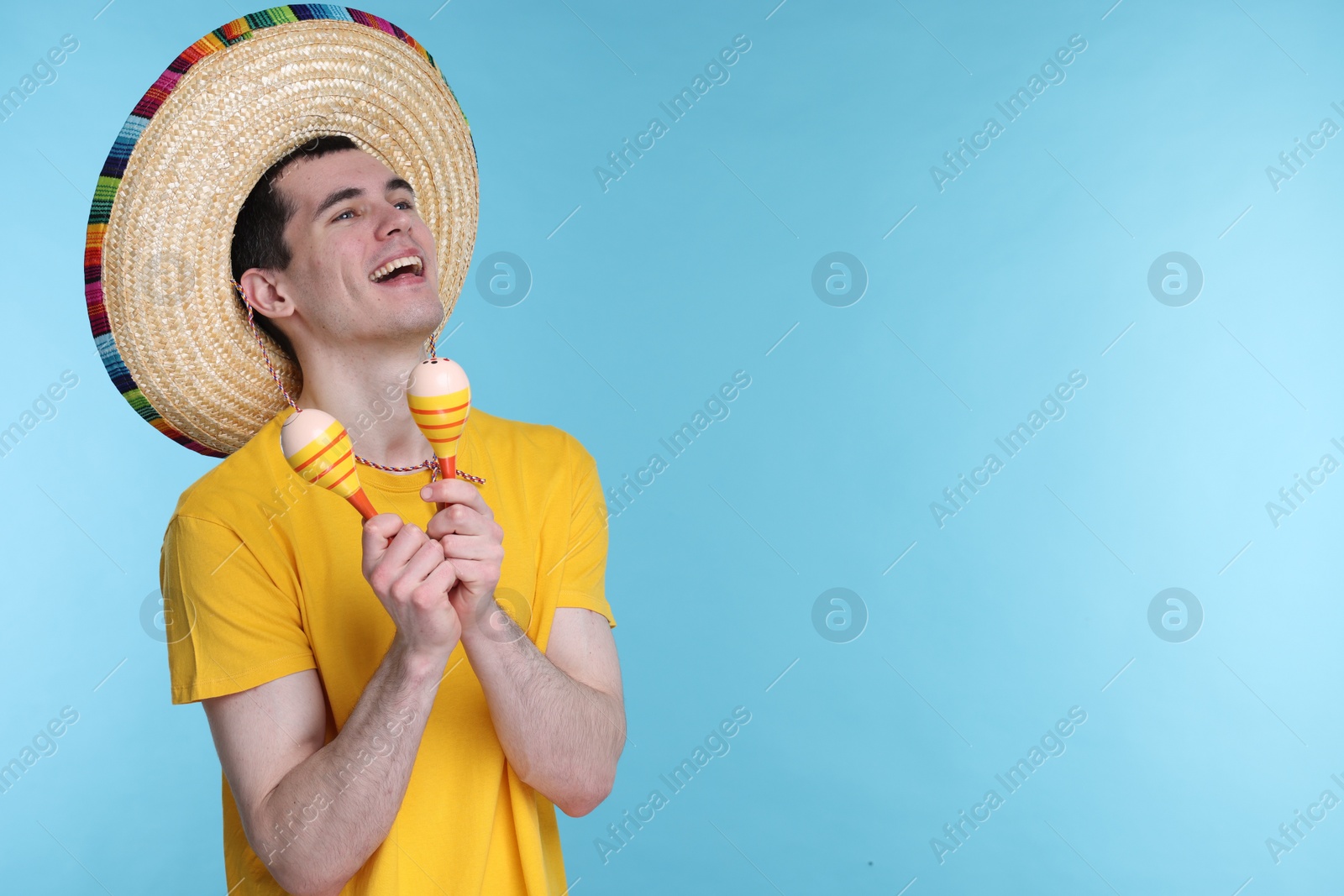 Photo of Young man in Mexican sombrero hat with maracas on light blue background. Space for text