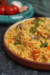 Photo of Delicious pilaf with meat and ingredients on black textured table, closeup