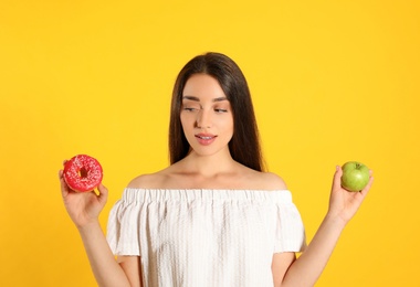 Woman choosing between apple and doughnut on yellow background