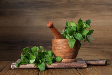 Photo of Mortar with pestle and fresh lemon balm on wooden table