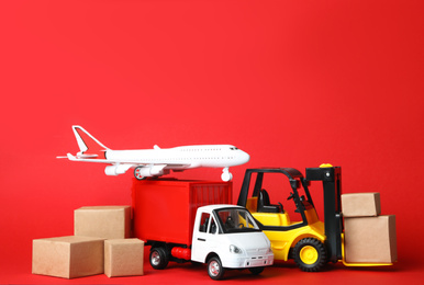 Photo of Different toy vehicles with boxes on red background. Logistics and wholesale concept