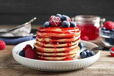 Delicious pancakes with fresh berries and syrup on wooden table