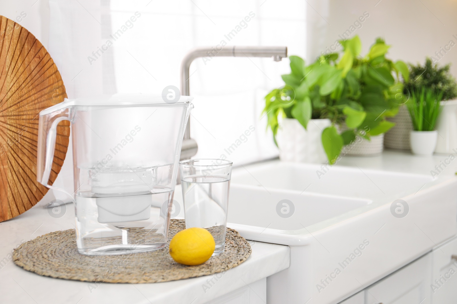 Photo of Water filter jug, glass and lemon on countertop in kitchen, space for text