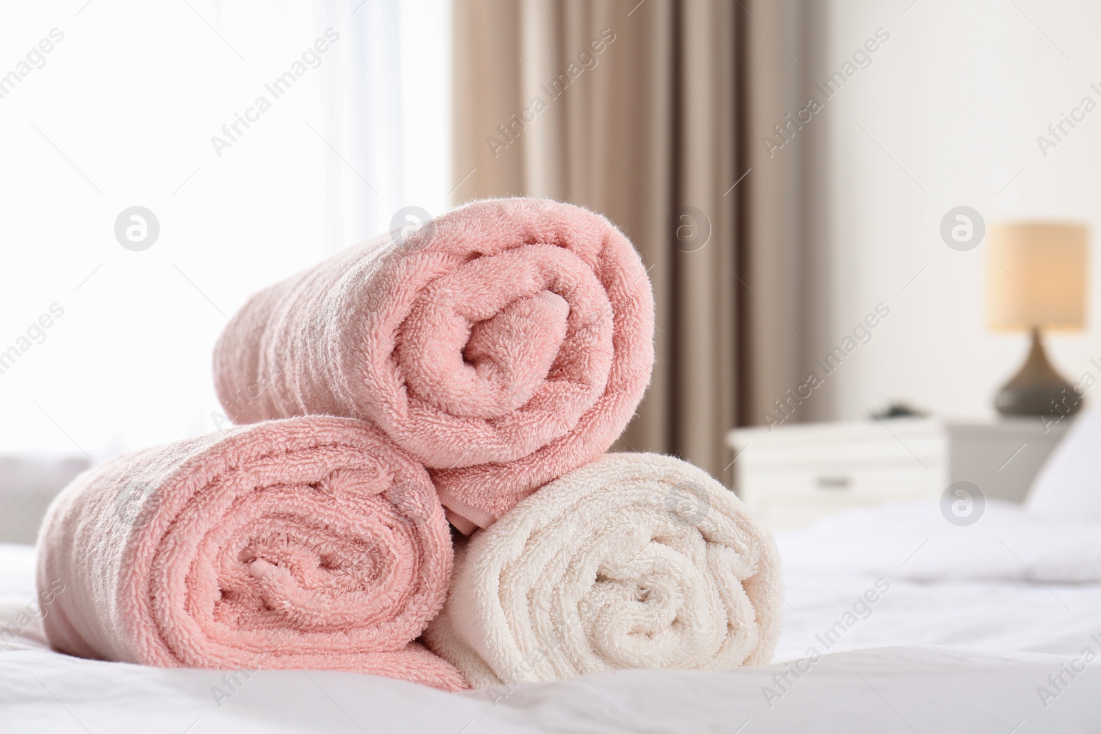 Photo of Rolled soft towels on bed in room. Space for text