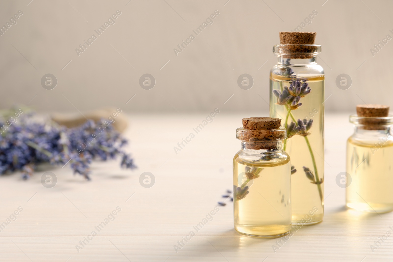 Photo of Essential oil and lavender flowers on white wooden table, closeup. Space for text