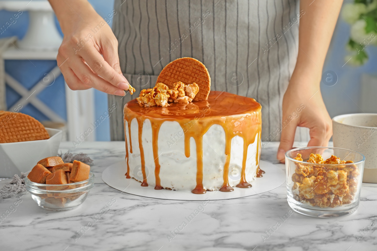 Photo of Young woman decorating delicious caramel cake at table