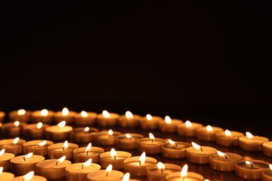 Photo of Burning candles on wooden table against black background