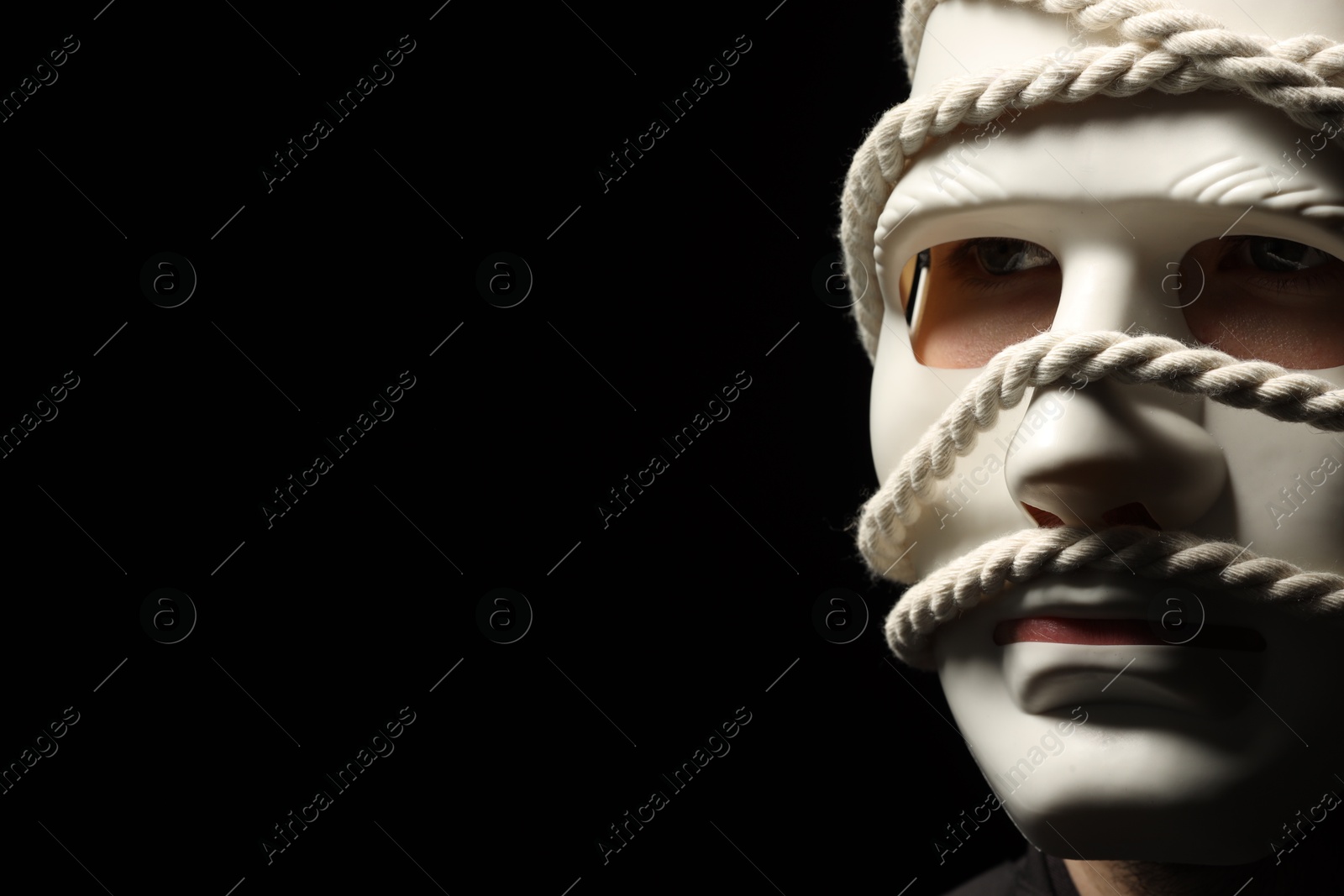 Photo of Theatrical performance. Man with plastic mask and hemp rope on black background, space for text