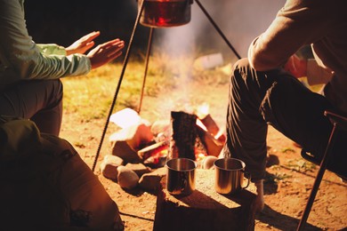 Photo of Couple warming hands near bonfire outdoors, closeup. Camping season