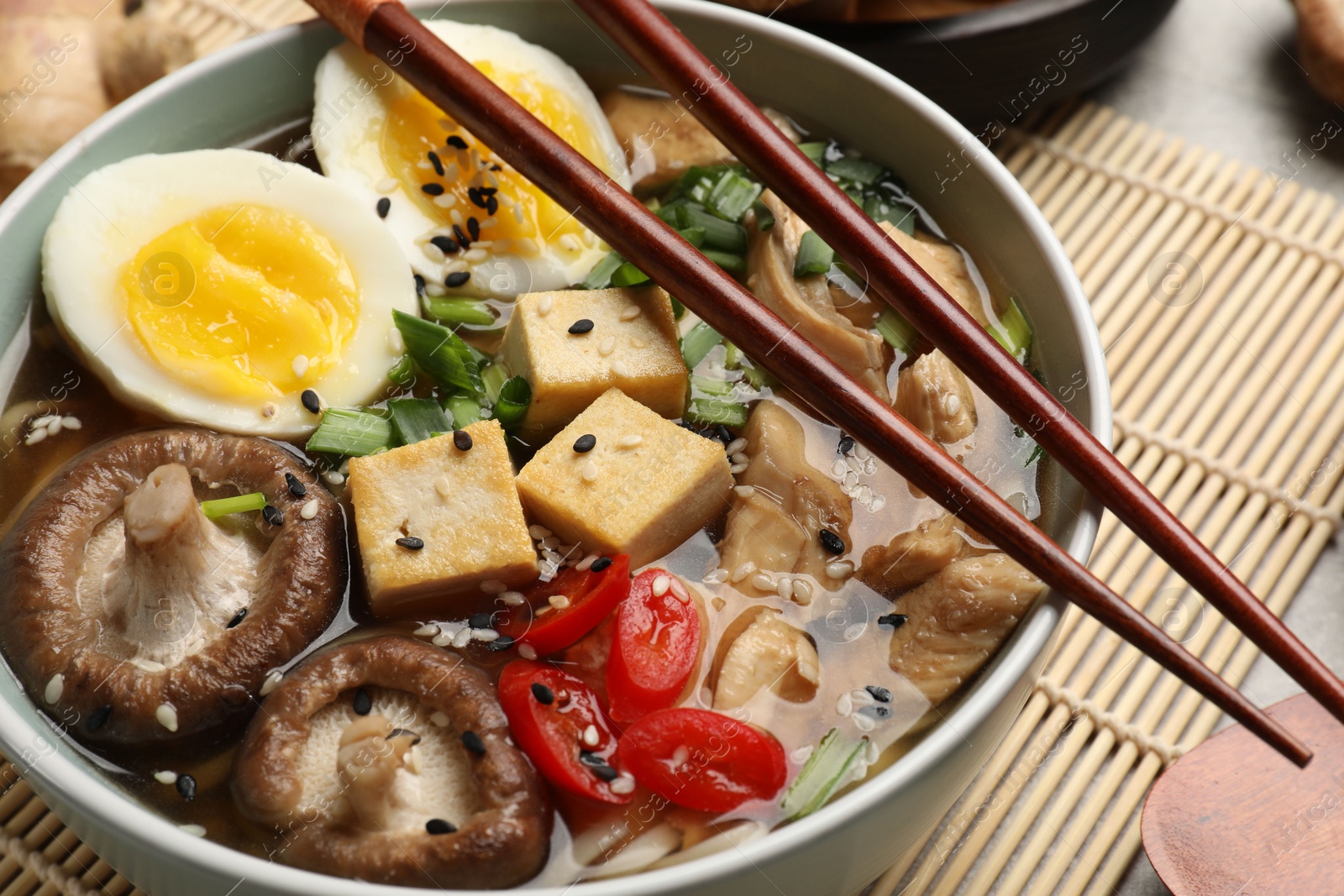 Photo of Bowl of delicious ramen and ingredients on grey table, closeup. Noodle soup