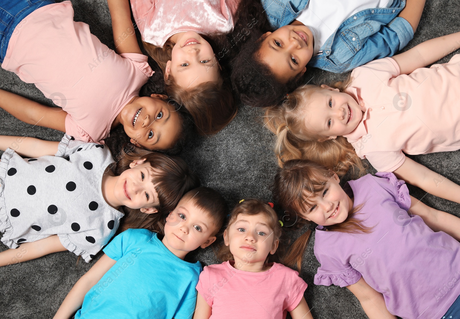 Photo of Adorable little children lying on floor together indoors, top view. Kindergarten playtime activities