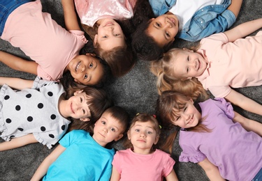 Photo of Adorable little children lying on floor together indoors, top view. Kindergarten playtime activities