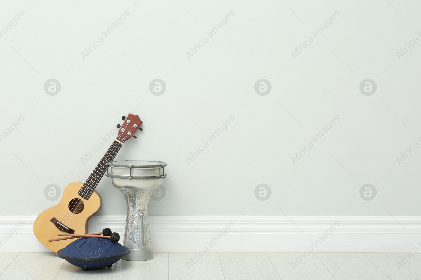 Photo of Ukulele and drums near white wall indoors, space for text. Musical instruments