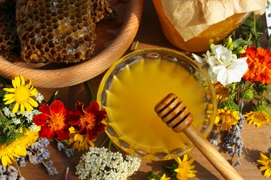 Photo of Delicious honey, combs and different flowers on wooden table, flat lay