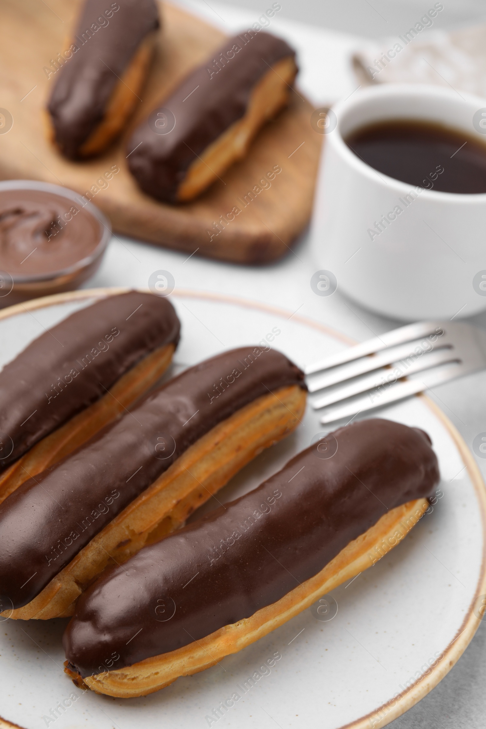 Photo of Delicious eclairs covered with chocolate on grey table, closeup