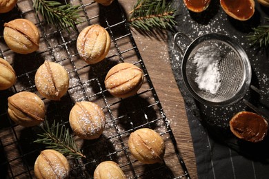 Delicious nut shaped cookies with powdered sugar and fir branches on wooden table, flat lay