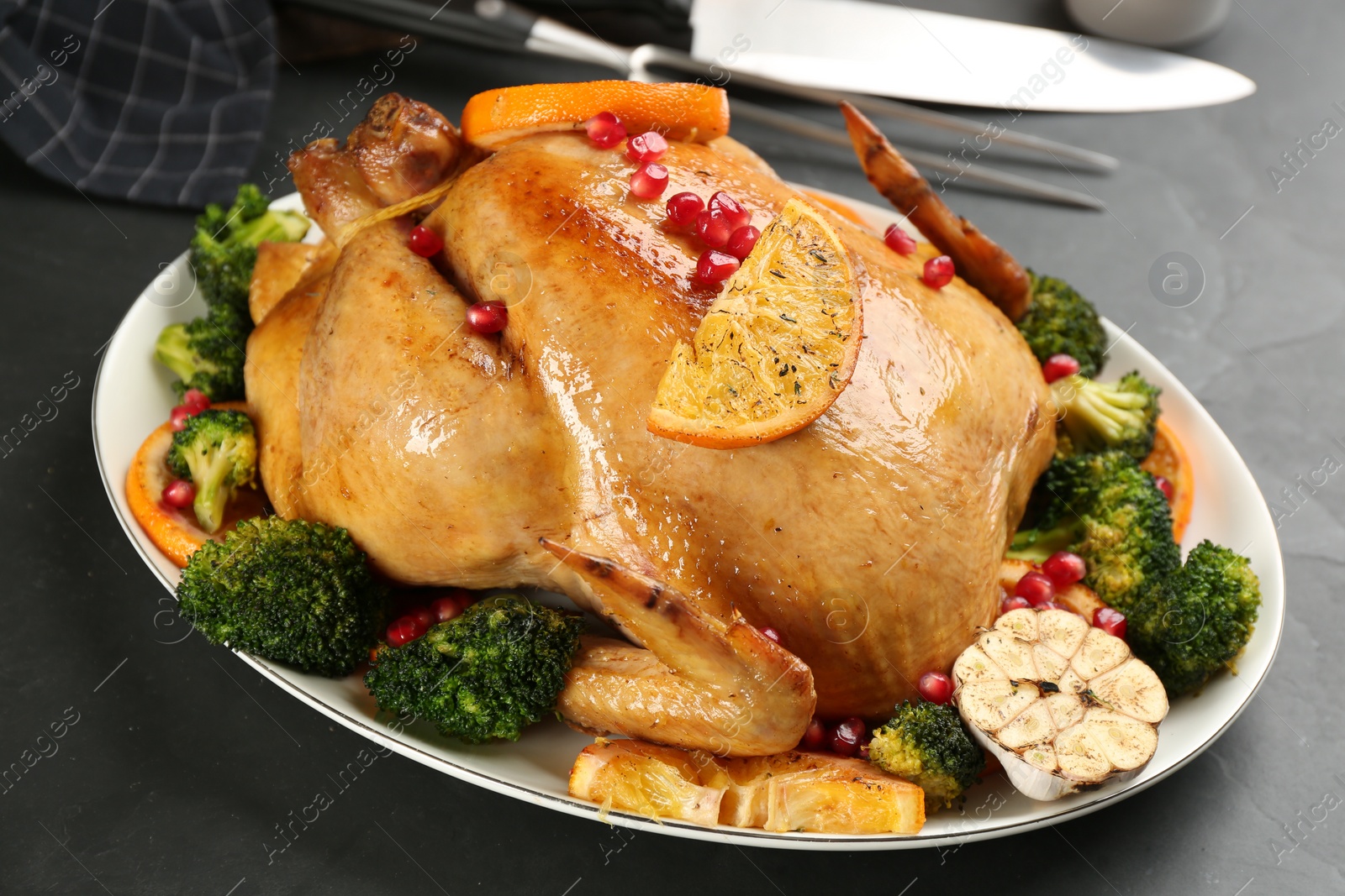 Photo of Delicious chicken with oranges, pomegranate and vegetables on black table, closeup