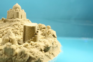Photo of Pile of sand with beautiful castle on light blue background, closeup. Space for text