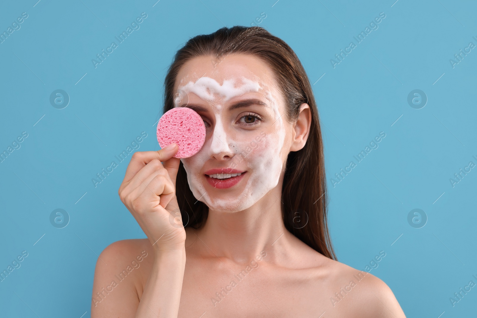 Photo of Happy young woman washing her face with sponge on light blue background