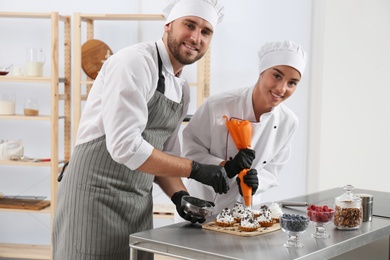 Photo of Pastry chefs preparing desserts at table in kitchen