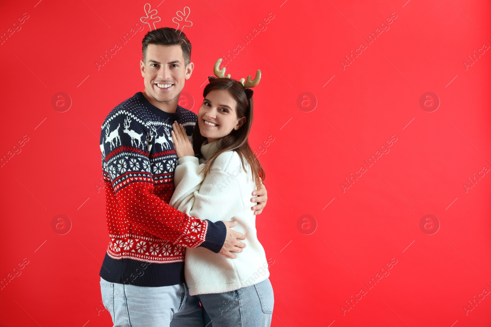 Photo of Beautiful happy couple in Christmas headbands and sweaters on red background. Space for text