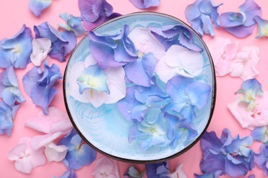 Spa composition. Aromatic water in bowl and flowers on pink background, flat lay