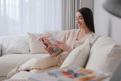 Photo of Young woman reading sports magazine on sofa at home