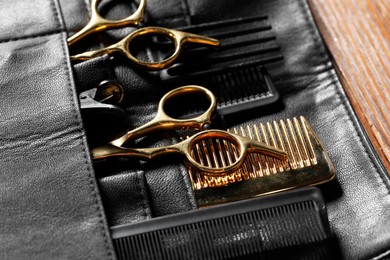 Hairdresser tools. Professional scissors and combs in leather organizer on wooden table, closeup