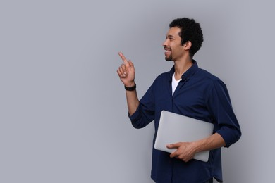Photo of Happy man with laptop pointing at something on grey background. Space for text