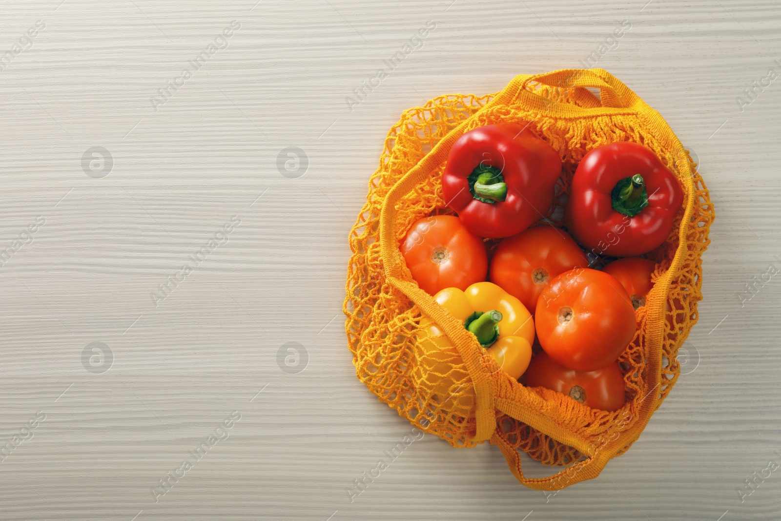 Photo of Net bag with vegetables on wooden table, top view. Space for text