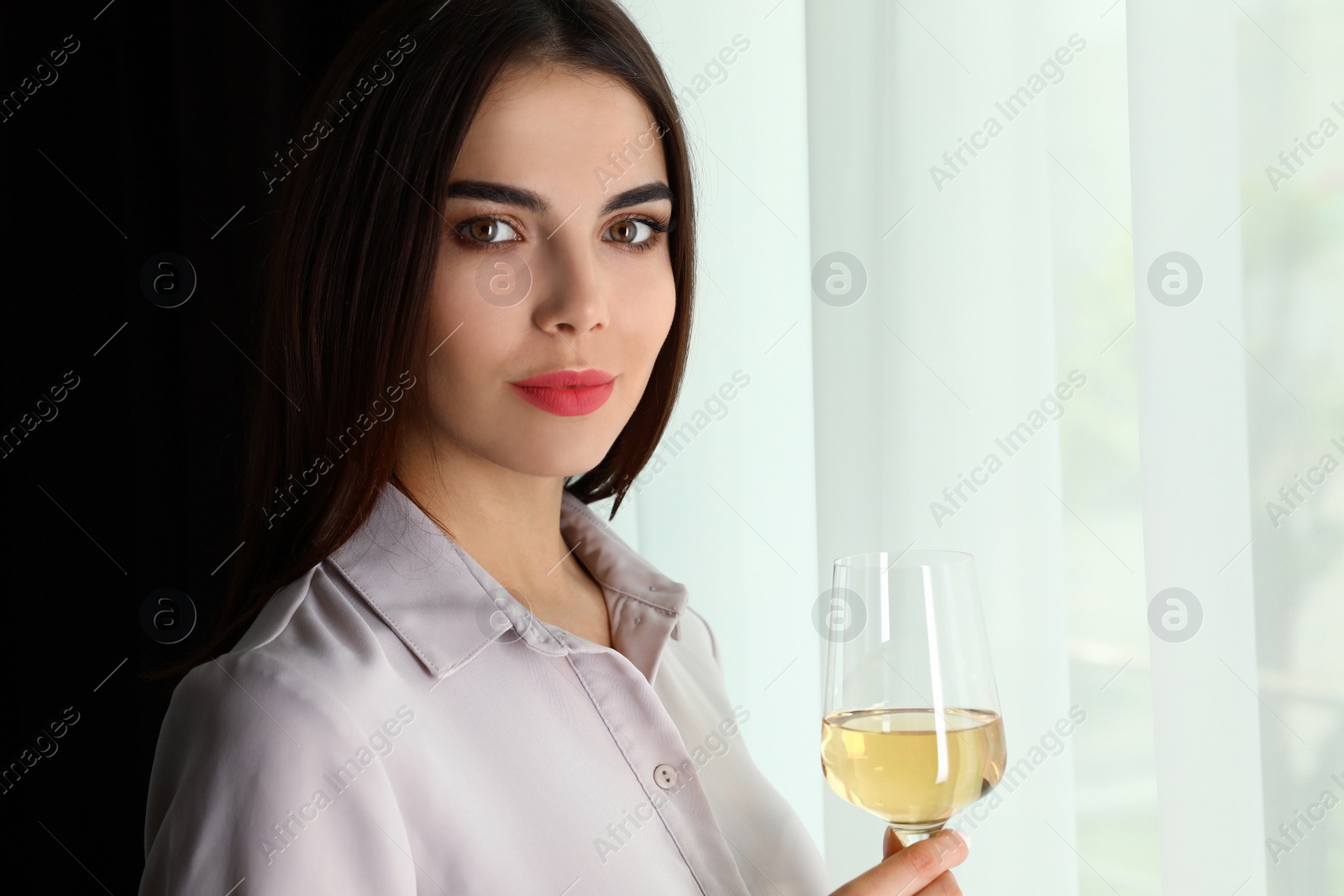 Photo of Beautiful young woman with glass of luxury white wine indoors. Space for text