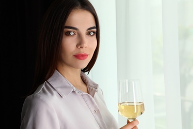 Photo of Beautiful young woman with glass of luxury white wine indoors. Space for text