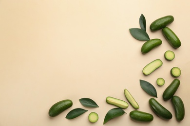 Whole and cut seedless avocados with green leaves on beige background, flat lay. Space for text