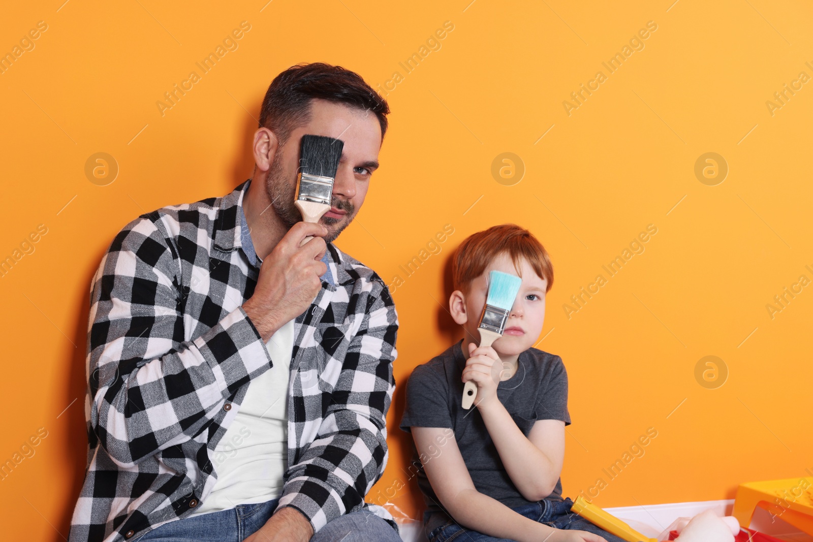 Photo of Father and son with brushes near orange wall. Repair work