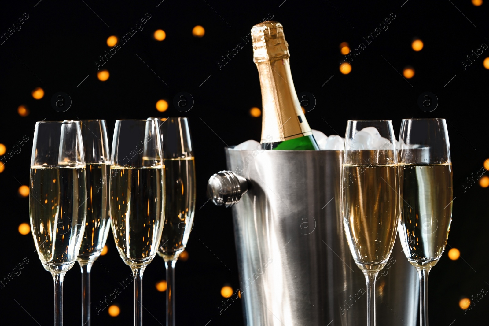 Photo of Glasses with champagne and bottle in bucket against blurred lights