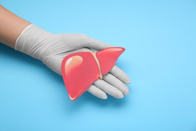 Doctor in glove holding paper liver on light blue background, closeup and space for text. Hepatitis treatment