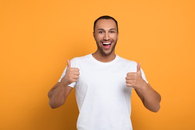 Photo of Smiling African American man showing thumbs up on orange background