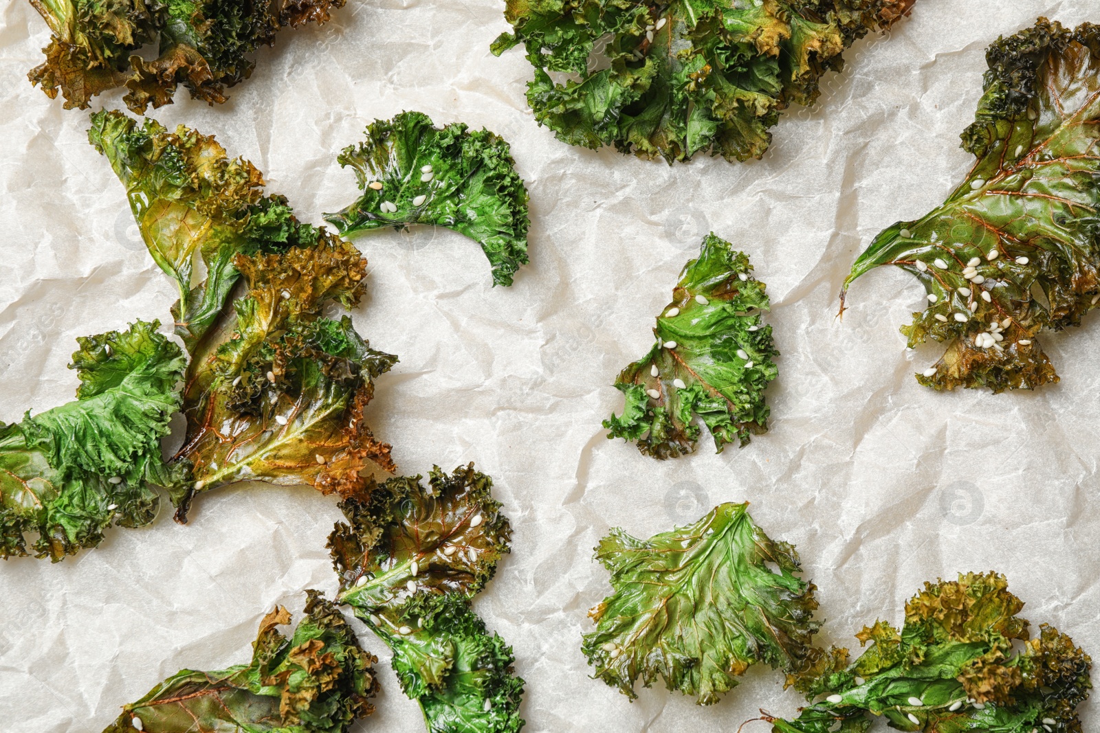 Photo of Tasty baked kale chips on parchment paper, flat lay