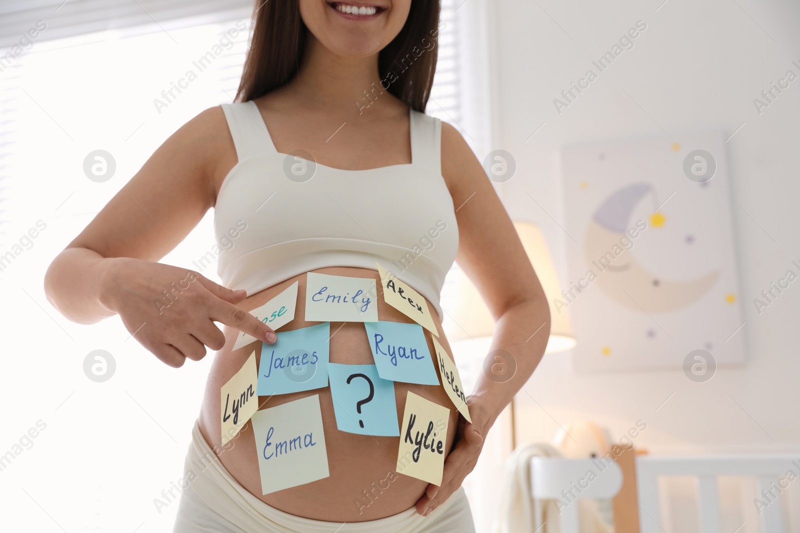 Photo of Pregnant woman with different baby names on belly at home, closeup. Space for text