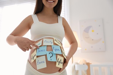 Photo of Pregnant woman with different baby names on belly at home, closeup. Space for text