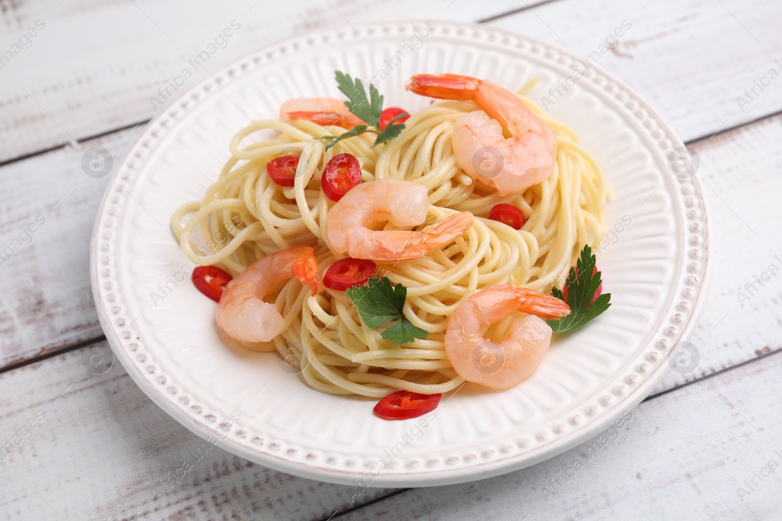 Photo of Tasty spaghetti with shrimps, chili pepper and parsley on wooden rustic table, closeup