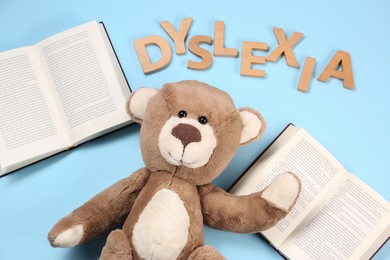 Photo of Word Dyslexia made of wooden letters, teddy bear and books on light blue background, flat lay
