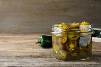 Photo of Glass jar with slices of pickled green jalapeno peppers on wooden table, space for text
